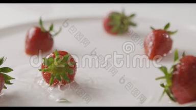 成熟的红色草莓果实落入一盘水的中心，溅起水花和水滴。 一些浆果